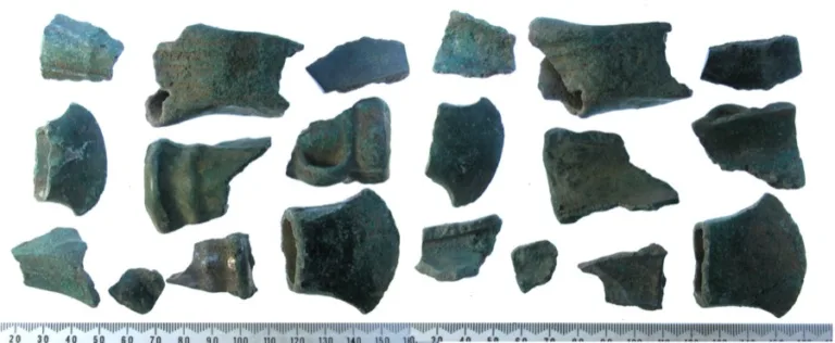 About twenty broken pieces of green corroded bronze laid out in rows above a scale bar.