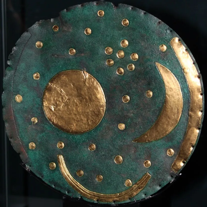 A blue-green bronze disc inlaid with a gold circle, a gold crescent and a scatter of gold dots.
