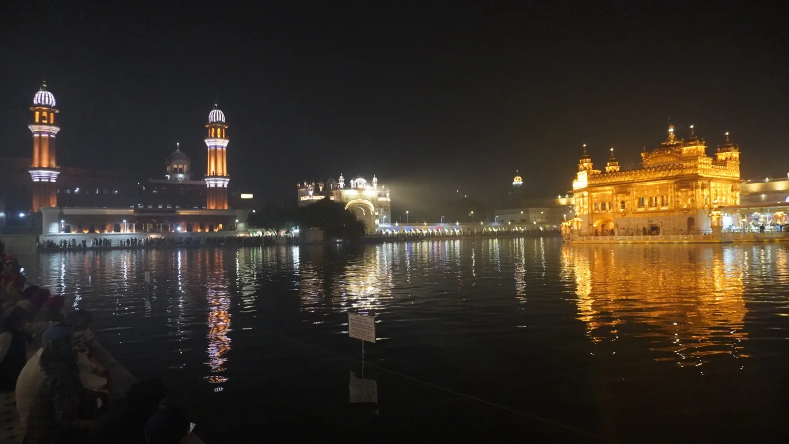 The Golden Temple in Amritsar lit up in gold at night, reflected in the still water of the pool around it.