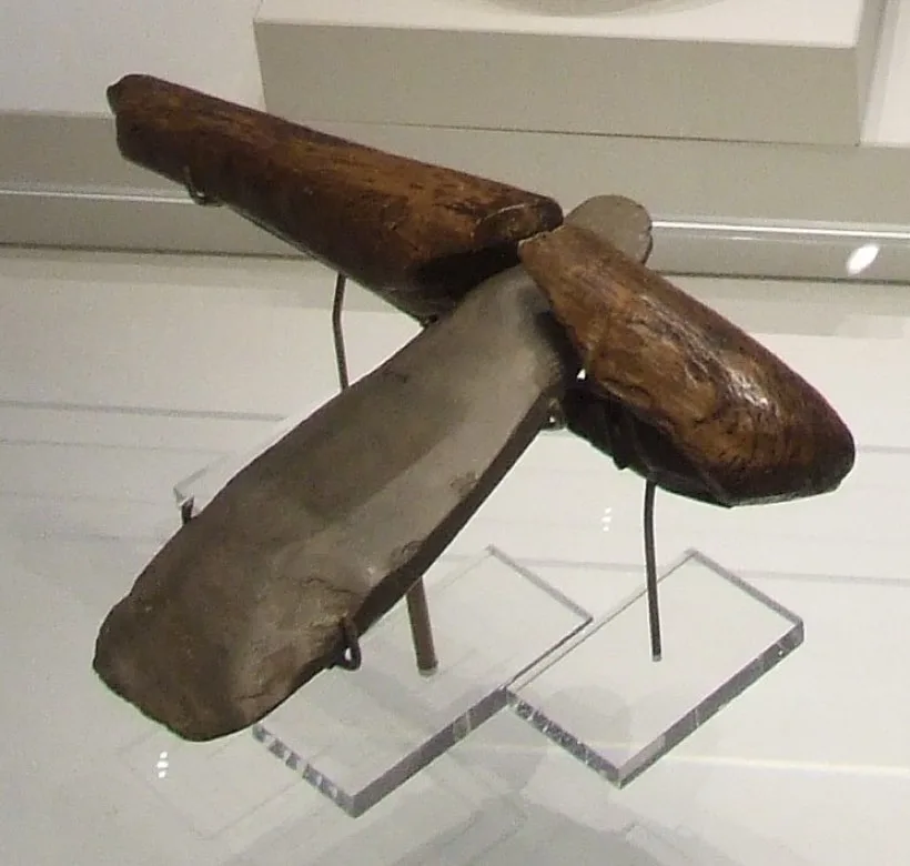 Two polished stone axe heads set into shaped wooden handles, displayed on stands.