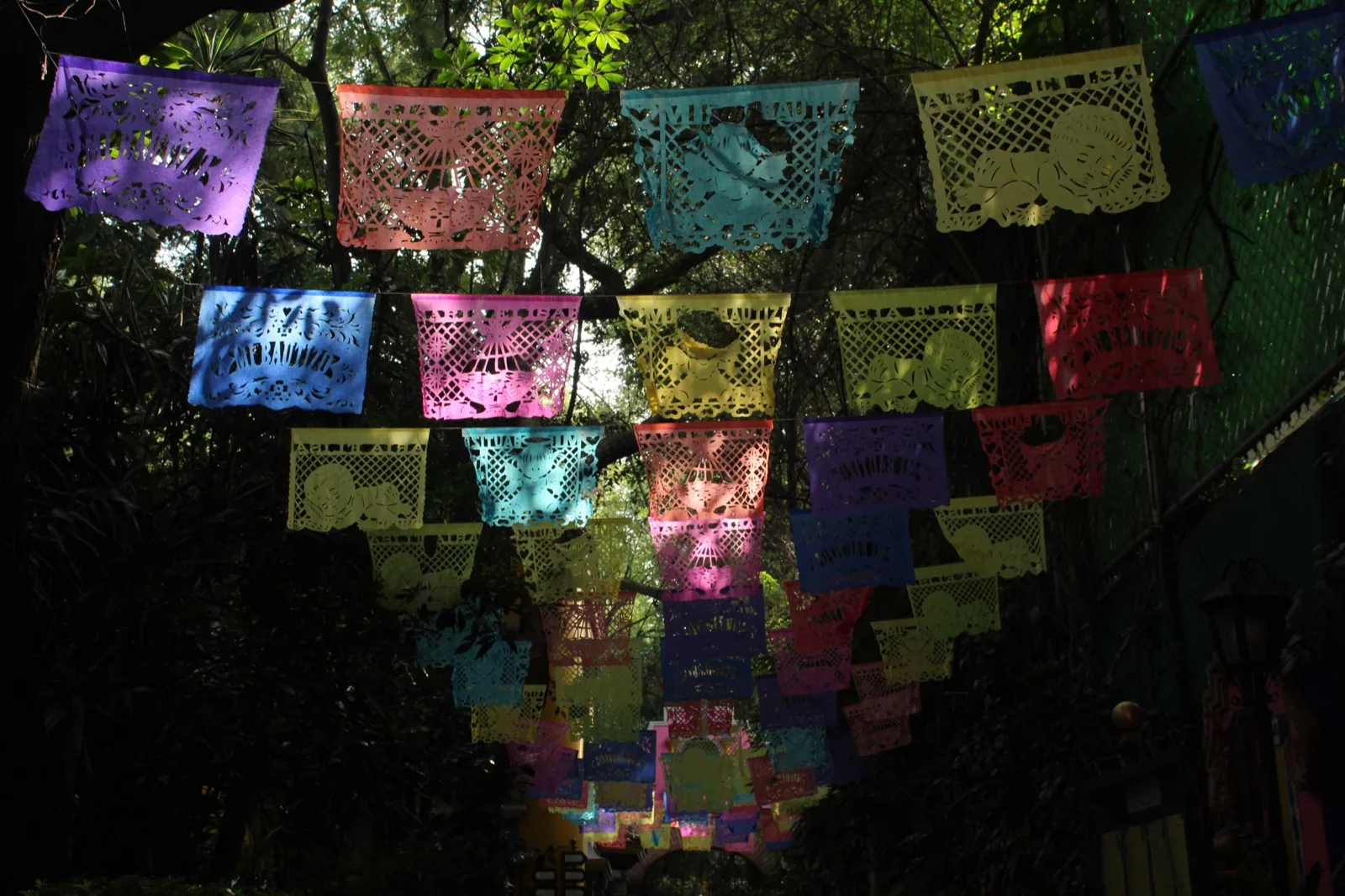 Rows of colourful cut-paper banners, called papel picado, hanging above a shady street.