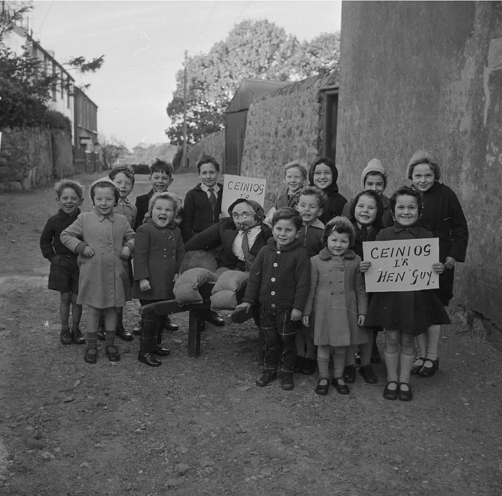A black-and-white photo of a group of children in 1962 standing around a stuffed guy, holding signs asking for pennies.